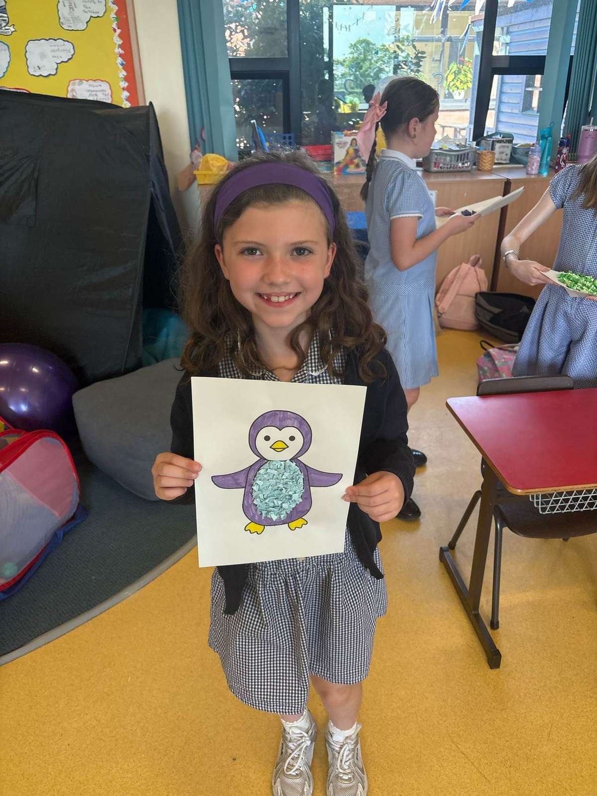 Child holding up a completed tissue-paper penguin craft during an art and craft club