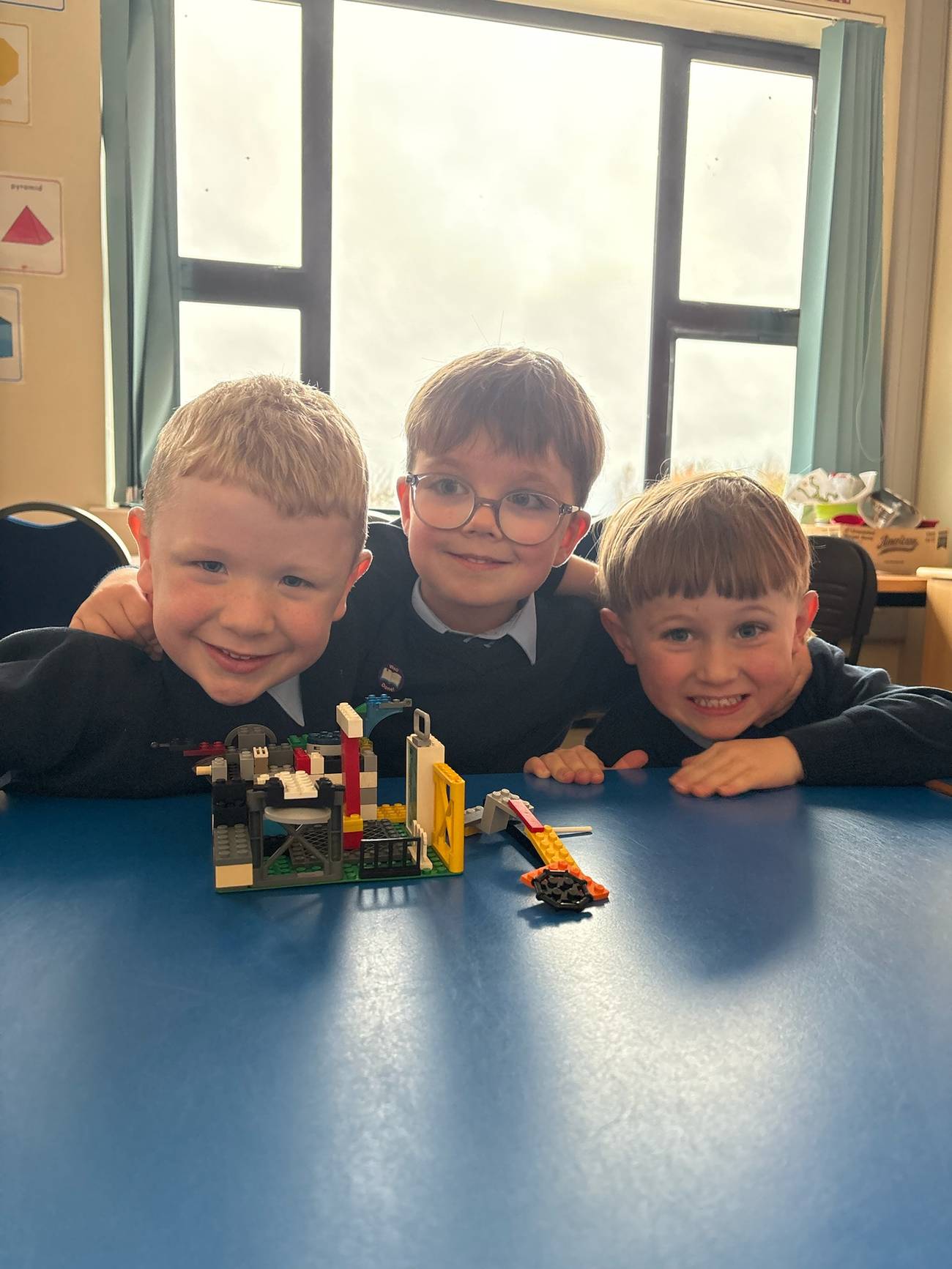 Children working together on a building activity, arms around each other