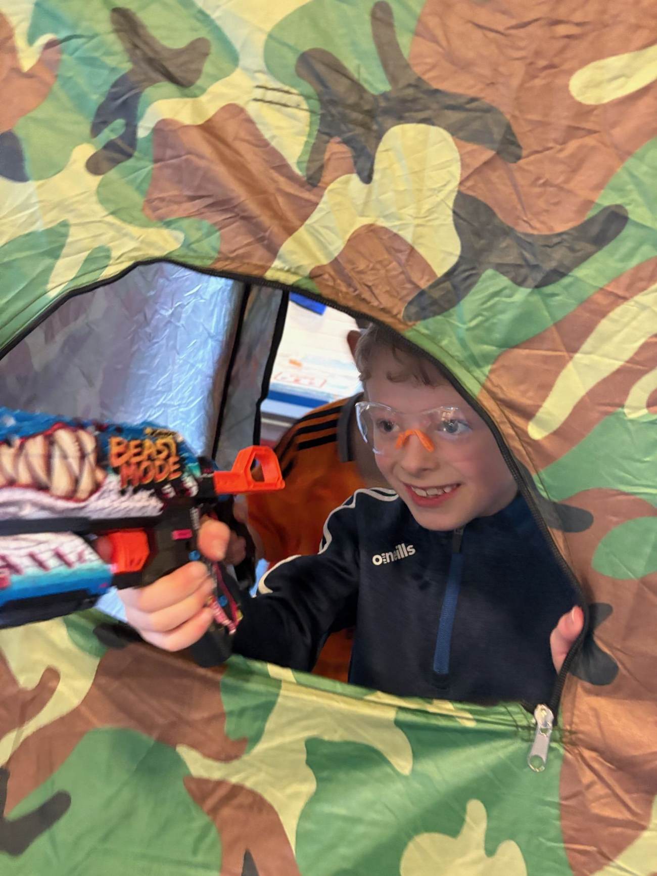 Child playing with a Nerf blaster inside a pop-up tent during an Elevate Sports party