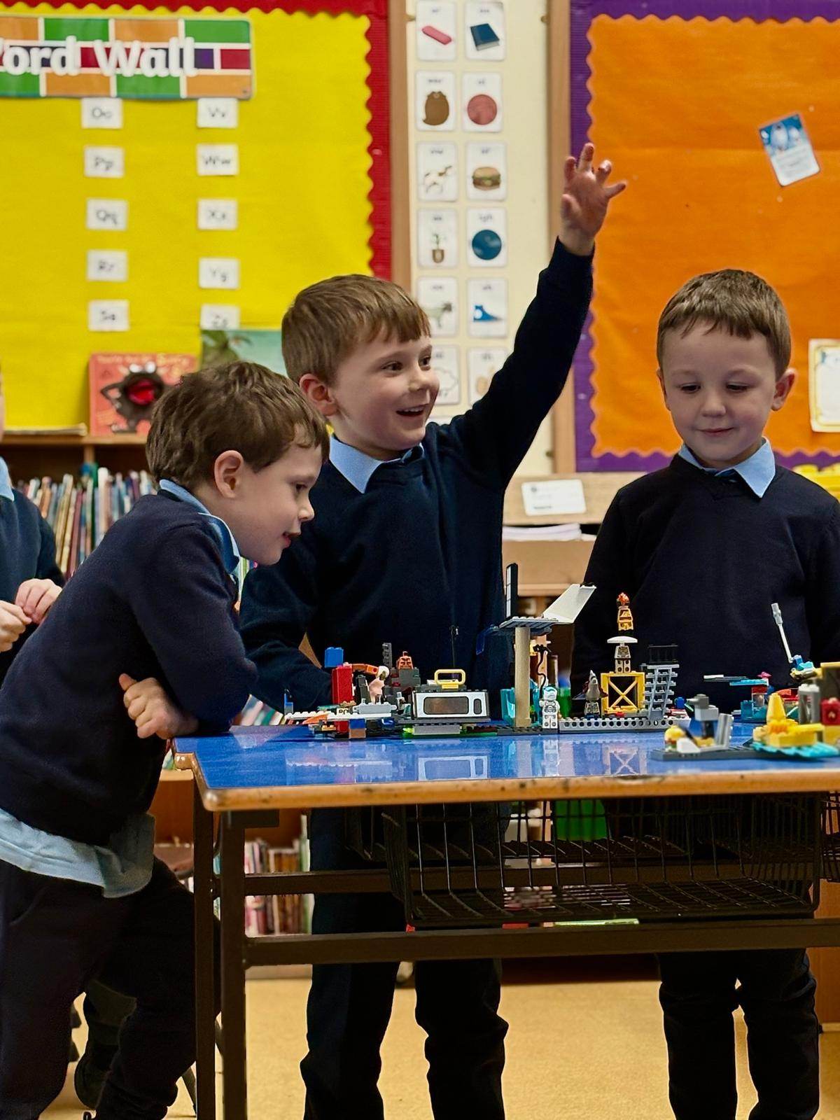 Children building with LEGO during an Elevate Sports after-school club, one raising his hand excitedly