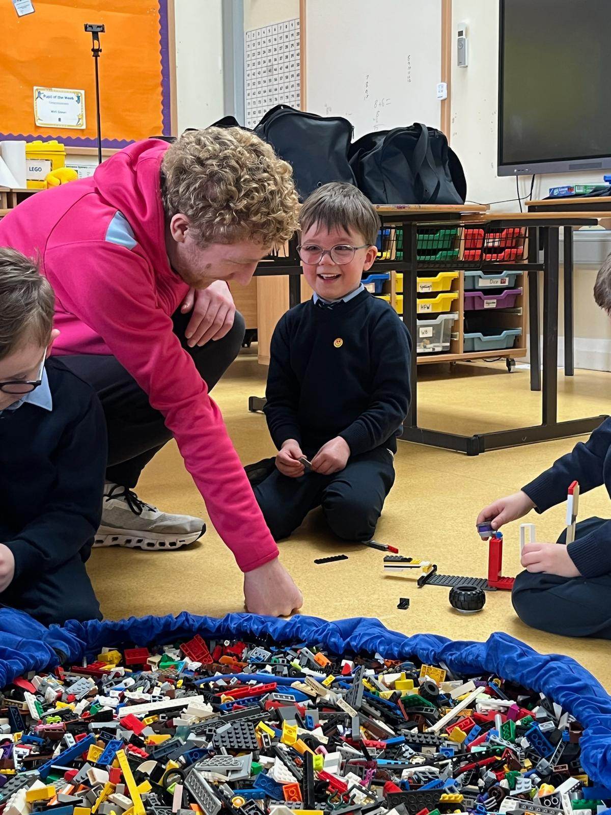 Elevate Sports coach kneeling with a child by a pile of LEGO, both smiling