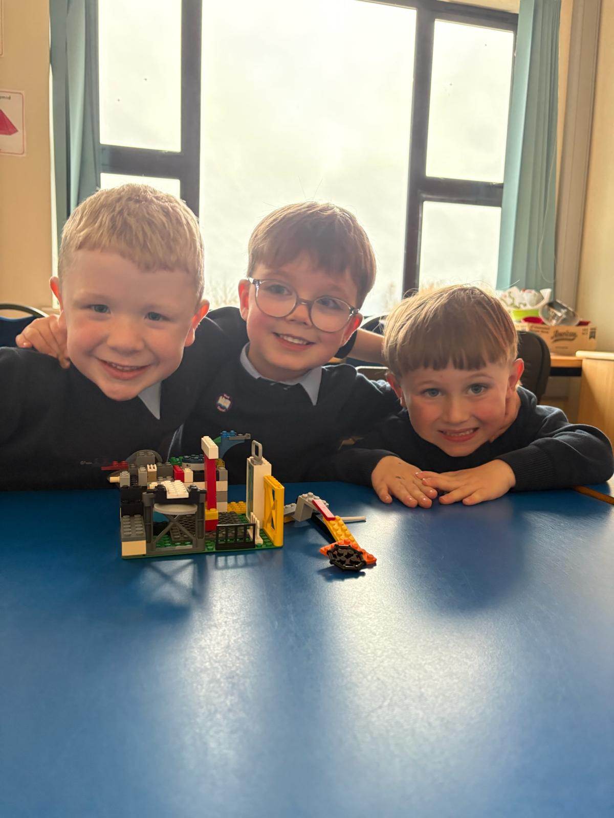 Three boys smiling together with their LEGO bridge build
