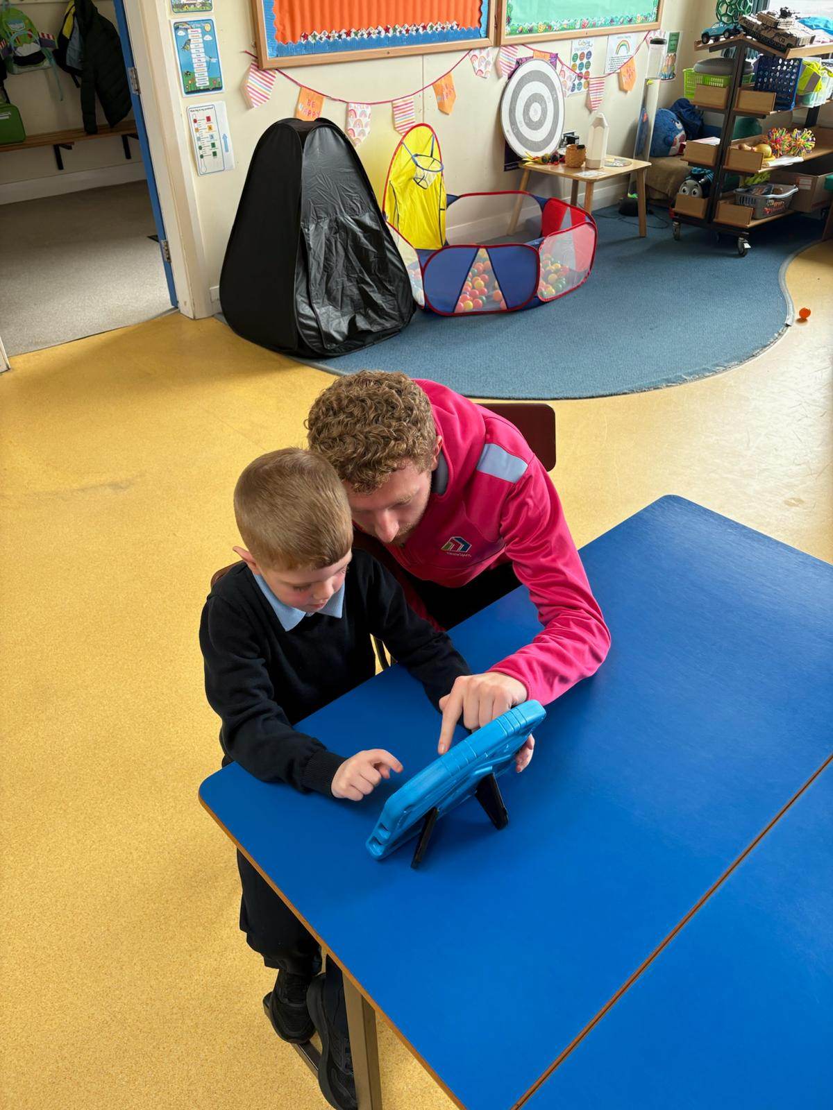 Elevate Sports coach helping a child one-to-one on a tablet during a STEM activity