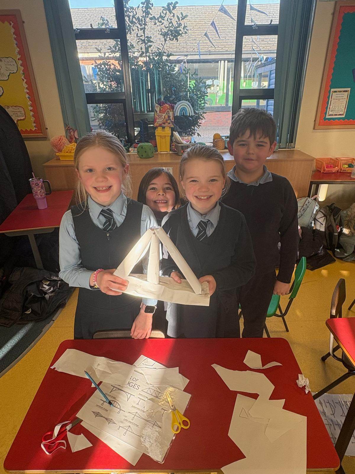 A group of children holding up their paper bridge build during a team building activity