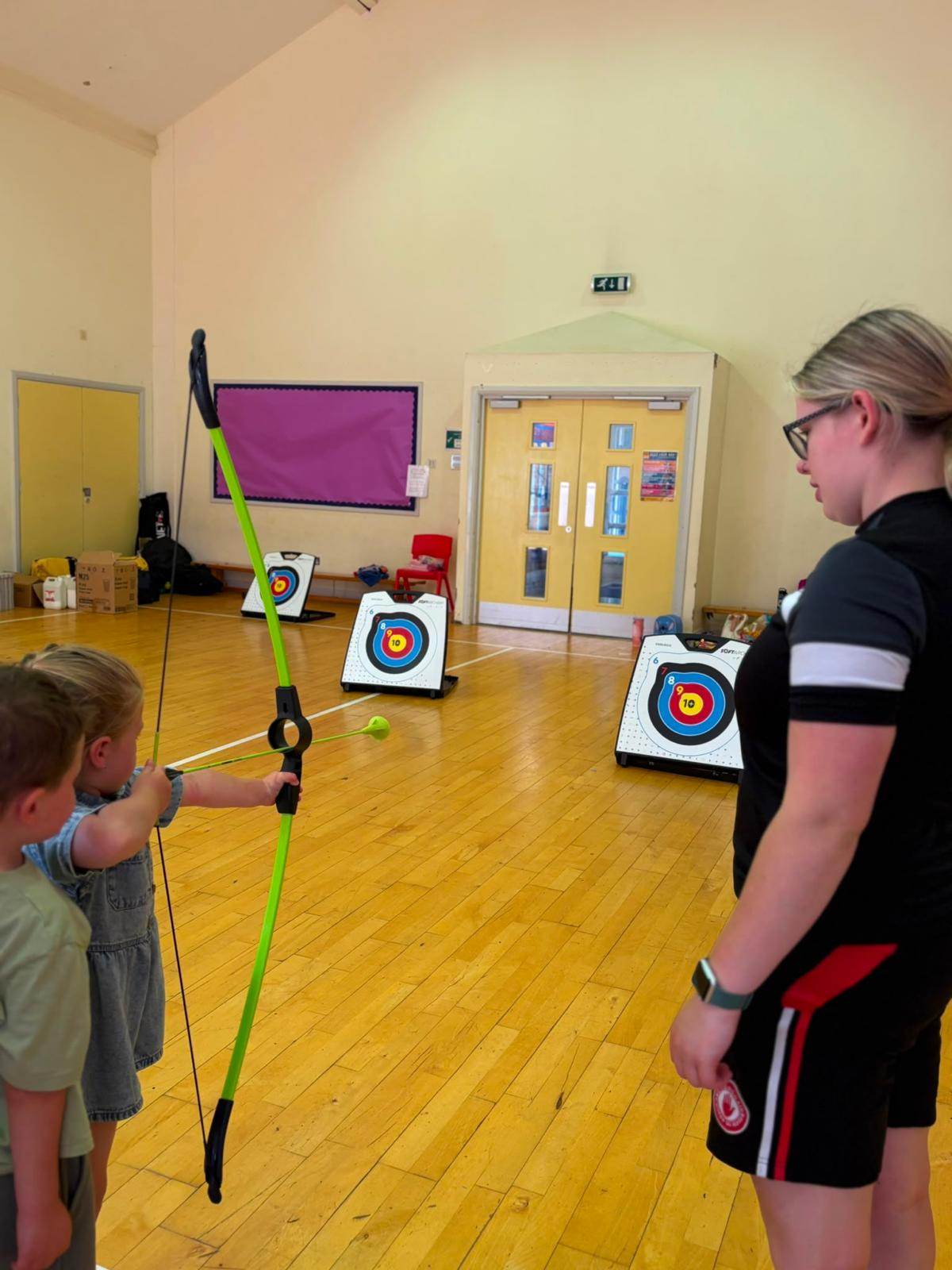 A coach supervising a child during an archery session as part of staff training