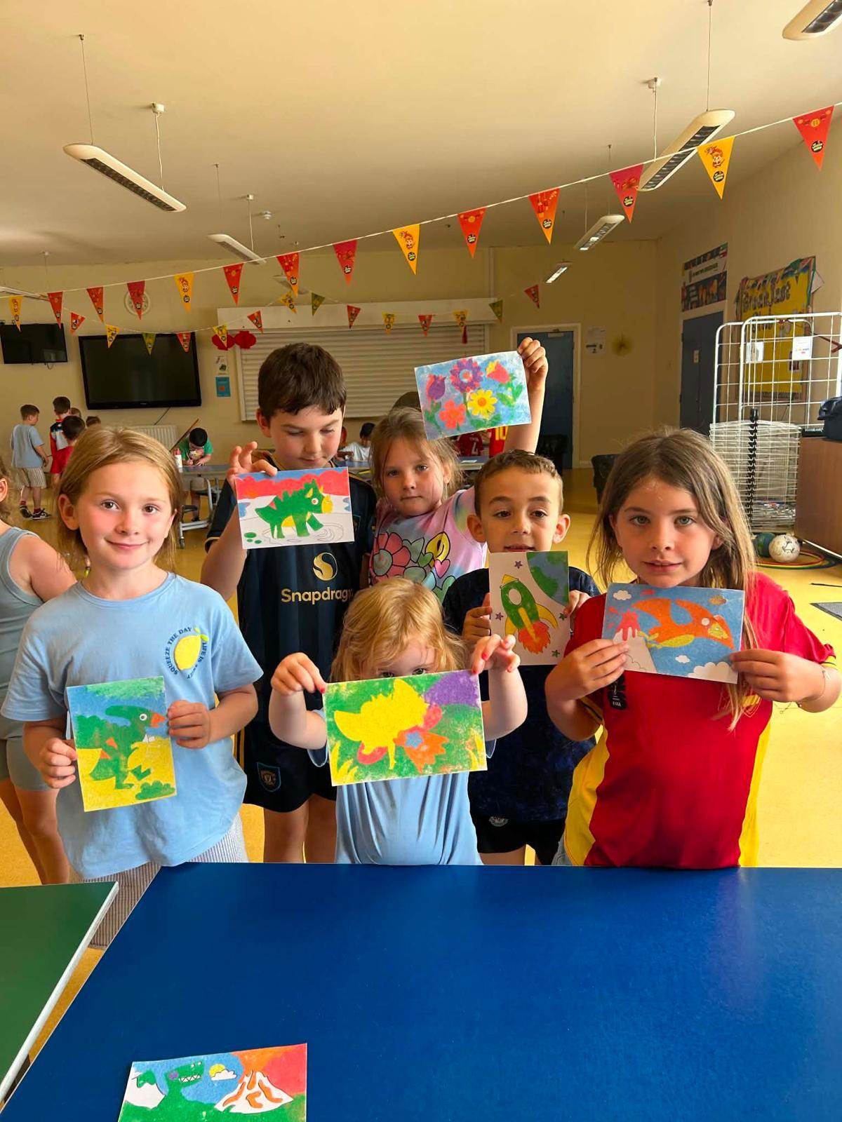 A group of children holding up their colourful artwork during an art and craft club